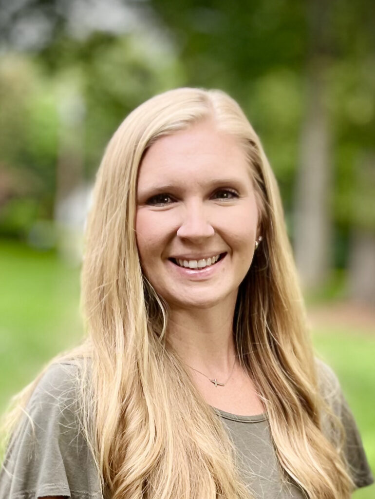 Smiling woman with long blonde hair outdoors in a green park.